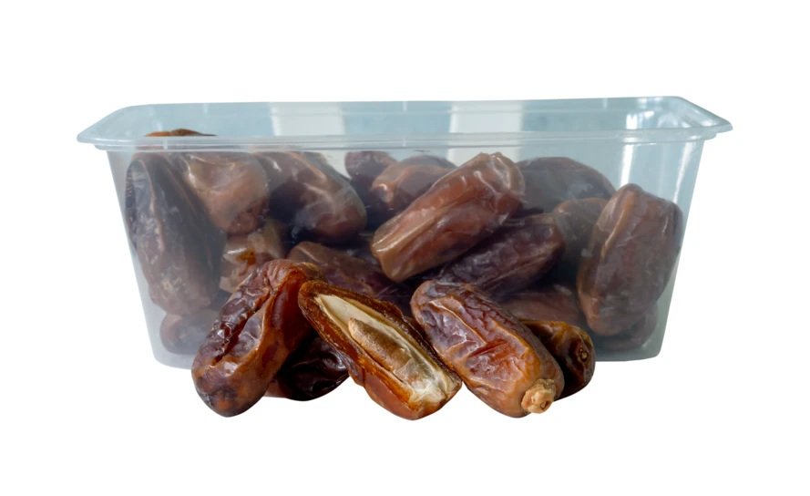 Dried dates in a clear plastic container on white background